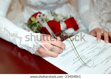 Bride with wedding bunch of flowers (bouquet) signing marriage lines (certificate).