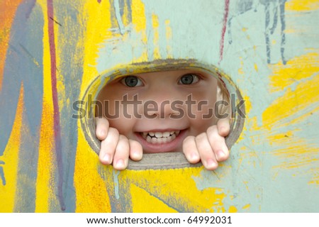 Pretty little girl smile and look out of the hole in painted wall.