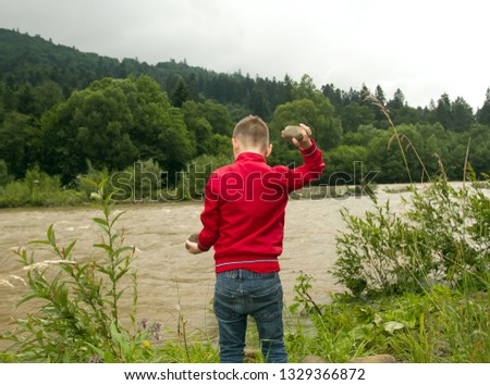 Boy Throw Stones In The River. Boy in red Jacket Throws Stones