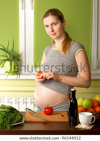 Pregnant woman on kitchen, eating tangerine