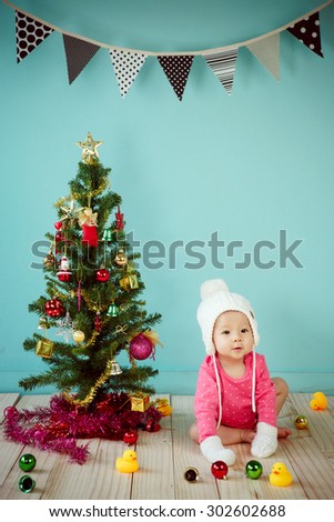 Infant child with white poodle hat and knitted mittens and Decorating Christmas tree on green background