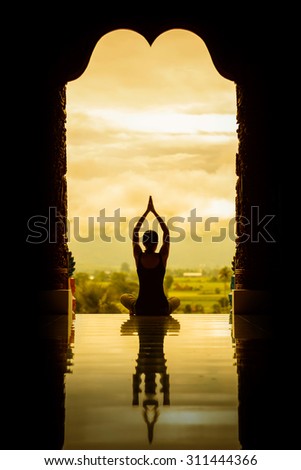 Yoga woman sitting in lotus pose on the temple during sunrise, with reflection in floor - vintage style color effect