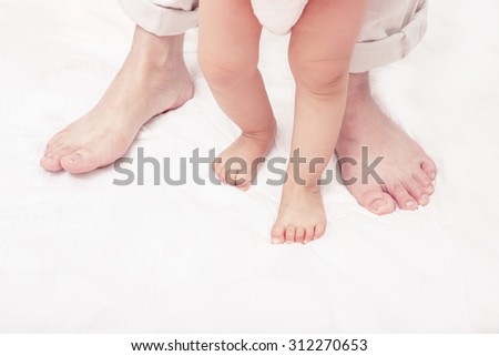 First steps. Baby learning to walk, with help of mothers and fathers. (Soft focus and blurry)