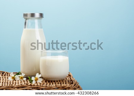 A bottle of milk and glass of milk on a wicker table on a blue background