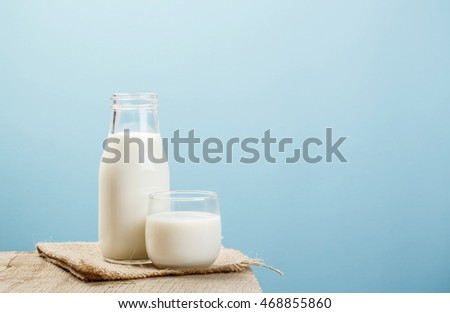 A bottle of rustic milk and glass of milk on a wooden table on a blue background, tasty, nutritious and healthy dairy products