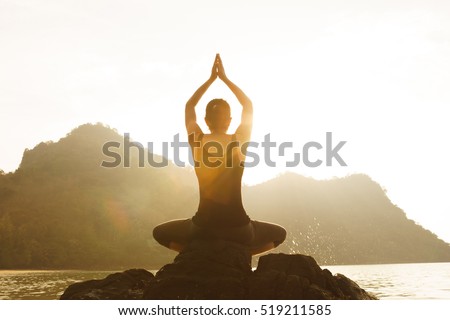 Yoga woman sitting in lotus pose on the beach during sunset (Lens Flare)