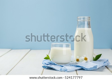 A bottle of milk and glass of milk on a white wooden table on a blue background, tasty, nutritious and healthy dairy products