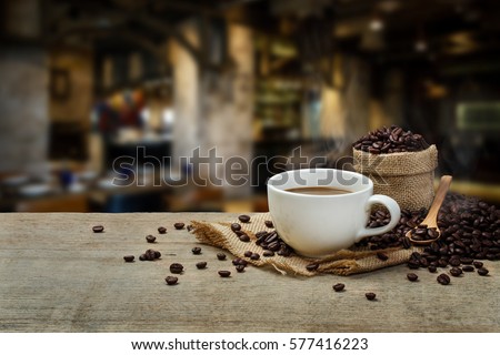 Hot Coffee cup with Coffee beans on the wooden table and the coffee shop background