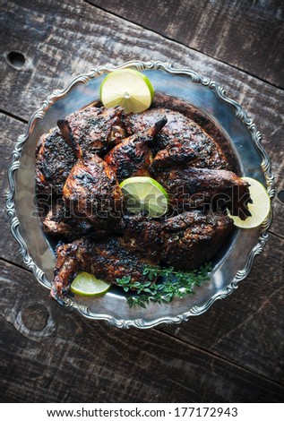Decorative silver platter of roasted chicken with jerk sauce, lime and herb garnish