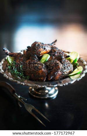 Decorative silver platter of roasted chicken with jerk sauce, lime and herb garnish