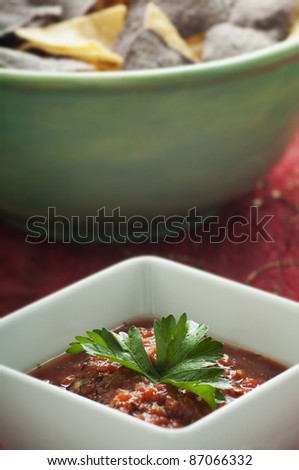 Green bowl of yellow and blue corn chips with fresh salsa on red cloth