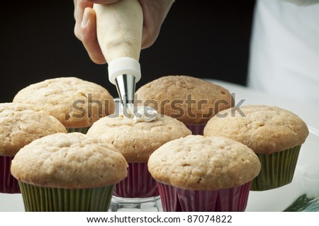 Golden cupcakes with butter cream being piped on by pastry chef/Fresh Baked Cupcakes