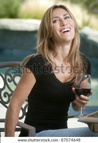 Woman siting by pool laughing and enjoying a glass of wine/Blond with Wine