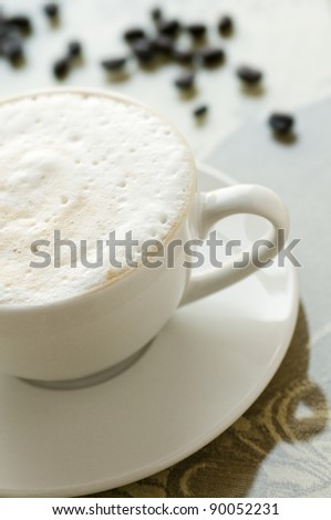 Cup of coffee with milk foam in white cup with saucer and beans