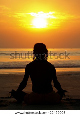 Silhouette of a man practicing yoga at sunset by the ocean