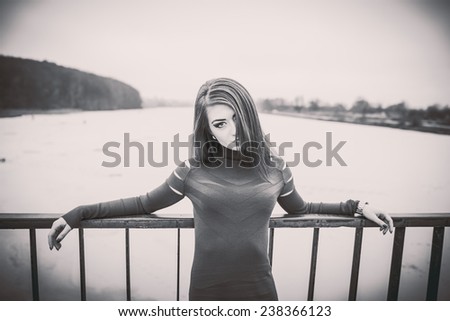 Young pretty sexy lady in black dress outdoor on the bridge with frozen lake on background, black and white