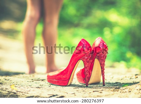 Red high heel shoes on the ground with barefoot girl on background
