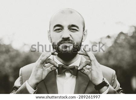 Man with beard in suit holding bow tie, grain effect
