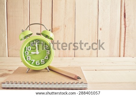 Alarm clock , notebook and pencil on wooden table over wood background, Still life style