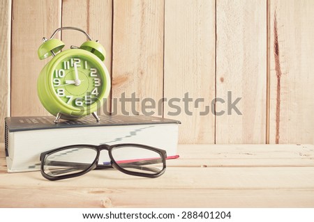 clock , eyeglasses and dictionary on wooden table over wood background, Still life style