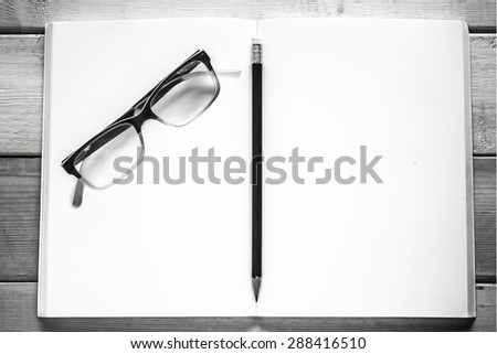 open notebook , pencil and eyeglasses on wood table ( black and white style )