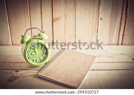 Alarm clock and notebook on wooden table over wood background, Still life style