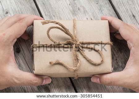 Hand hold A Vintage gift box brown paper wrapped with rope on wood background