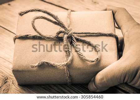 Hands hold A Vintage gift box brown paper wrapped with rope on wood background , antique tone