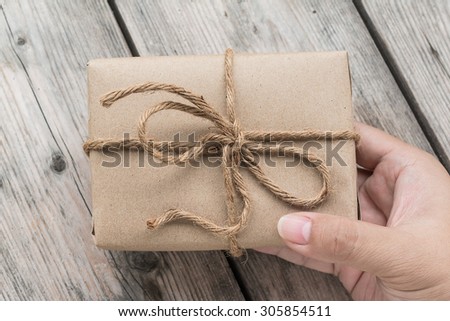 Hands hold A Vintage gift box brown paper wrapped with rope on wood background