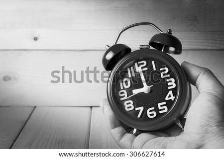 Hand hold alarm clock on wood background , black and white tone