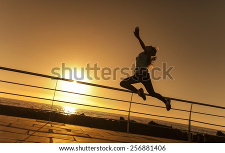 Jumping young woman near the ocean at the sunset