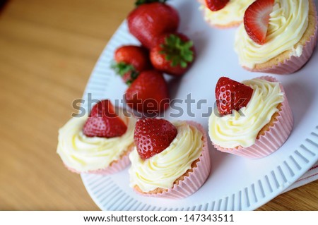 Closeup shot of fresh vanilla cream and strawberry cupcakes on a wooden kitchen table