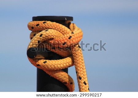 Yellow rope with black flecks tied around a large black post symbolizing boating, yachting and security