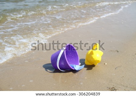 Children\'s toys on the beach on the river bank. Baby bucket, rake and watering can. Waves estuary.