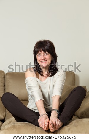 woman sitting on the sofa point that grabs your feet with your hands while smiles