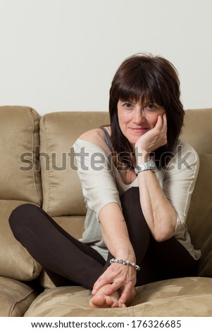 woman sitting on the sofa looking directly at the camera and grabs the feet with one hand