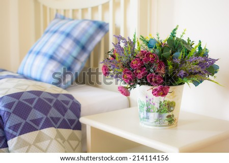 Vase of flowers on a side table near a bed.