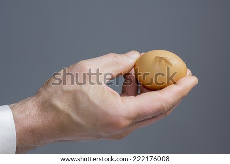 A male hand with the hen egg and feather./	Hens egg with a signature