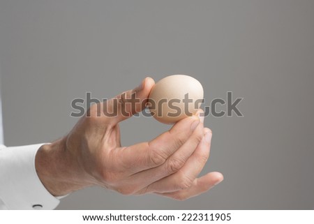 Close view of male\'s right hand with one hen\'s egg./ Male\'s hand with hen\'s egg.