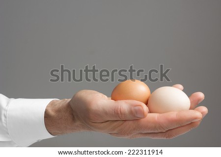 Close view of male\'s right hand with two hen\'s eggs./ Male\'s hand with hen\'s eggs.
