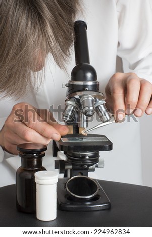 Men working with an old microscope, tweezers and a two bottles