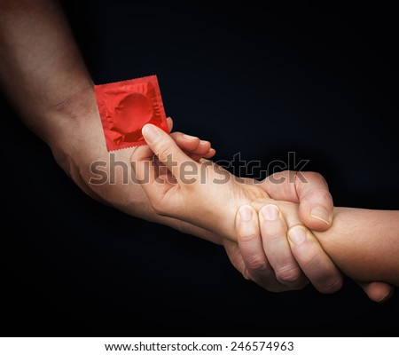 Man\'s hand holding woman hand with a red condom in a black background