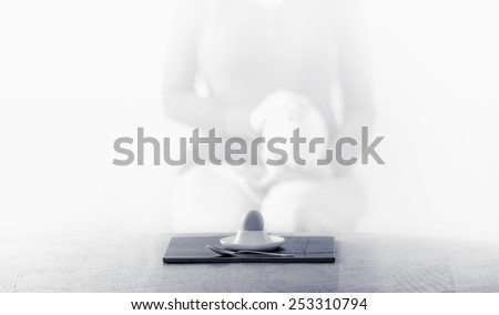 Woman\'s silhouette with ostrich egg near a table with an eggcup and a hen\'s egg in black white