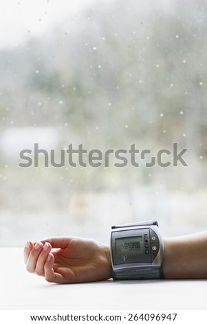 Woman\'s hand with blood pressure measuring device showing low blood pressure near a window in winter