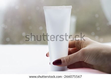 Woman hand with white cream tube in a bright background