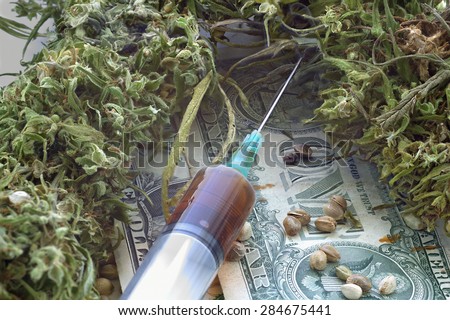 Syringe with brown liquid and hemp seeds and dried hemp leaves on dollar banknotes