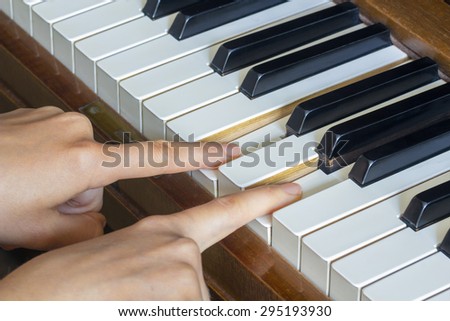 Close view of  girl\'s hands two fingers holding pressed  keys on a piano