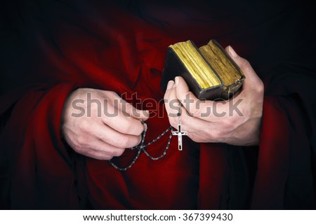 Mystery monk with a cape holding bibles and a black rosary in his hands
