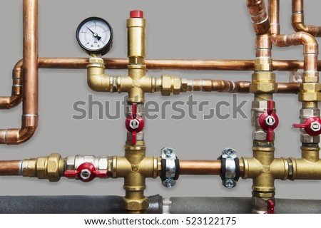 Heating system\'s cooper pipes with ball valves and manometer on a grey wall