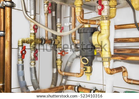 Heating system\'s copper pipes with ball valves on a white wall.